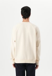 Felpa beige con scollo rotondo, maniche raglan e polsini a coste. Texture morbida, vestibilità rilassata e design minimalista.
