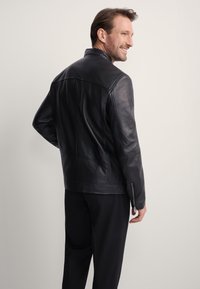 Czarna skórzana kurtka z wysokim kołnierzem i dopasowanym krojem. Z widocznymi szwami na ramionach i zapinanymi na zamek mankietami. Gładka tekstura.