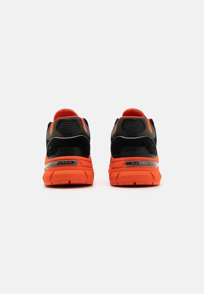 Schwarze und orange Sport Schuhe mit einer runden Silhouette, Obermaterial aus Wildleder und Mesh, strukturiertem Fersenbereich sowie Logo-Details an der Seite und Ferse.