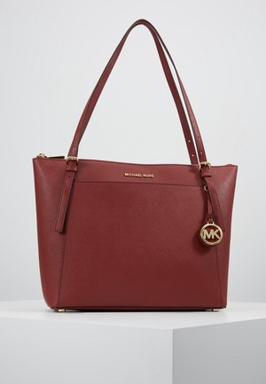 Sac cabas Michael Kors rouge foncé avec doubles bretelles, breloque logo dorée et surface en cuir texturé sur une plateforme blanche.