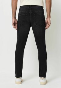 Jeans negre din denim cu o croială slim, având două buzunare la spate și o textură netedă. Asociate cu sneakers albi și un top de culoare deschisă.