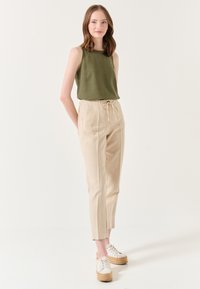 Olivegrünes ärmelloses Top, beige Leinenhose mit Kordelzug und Keil-Esparilles. Glattes Material mit einem lässigen Schnitt und schmal zulaufenden Knöcheln.