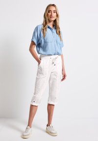 Lichtblauw kortnekkig overhemd met knopen en twee borstzakken, gecombineerd met witte cropped broek met een elastische tailleband en koord.