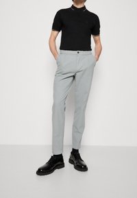 Svart polo med kort ärm, grå smal passform byxor och glänsande svarta snörskor med en strukturerad sula.