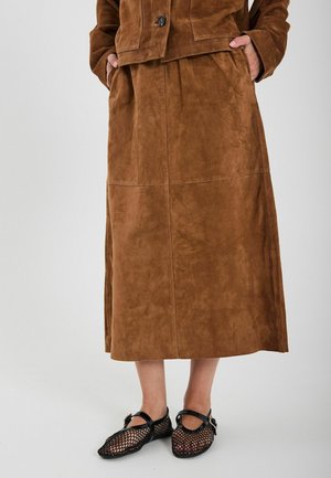 Brauner Wildledermaxirock mit glatter Textur, mit Seitentaschen und lässiger Passform. Kombiniert mit schwarzen Netzschuhen mit Knöchelriemen.