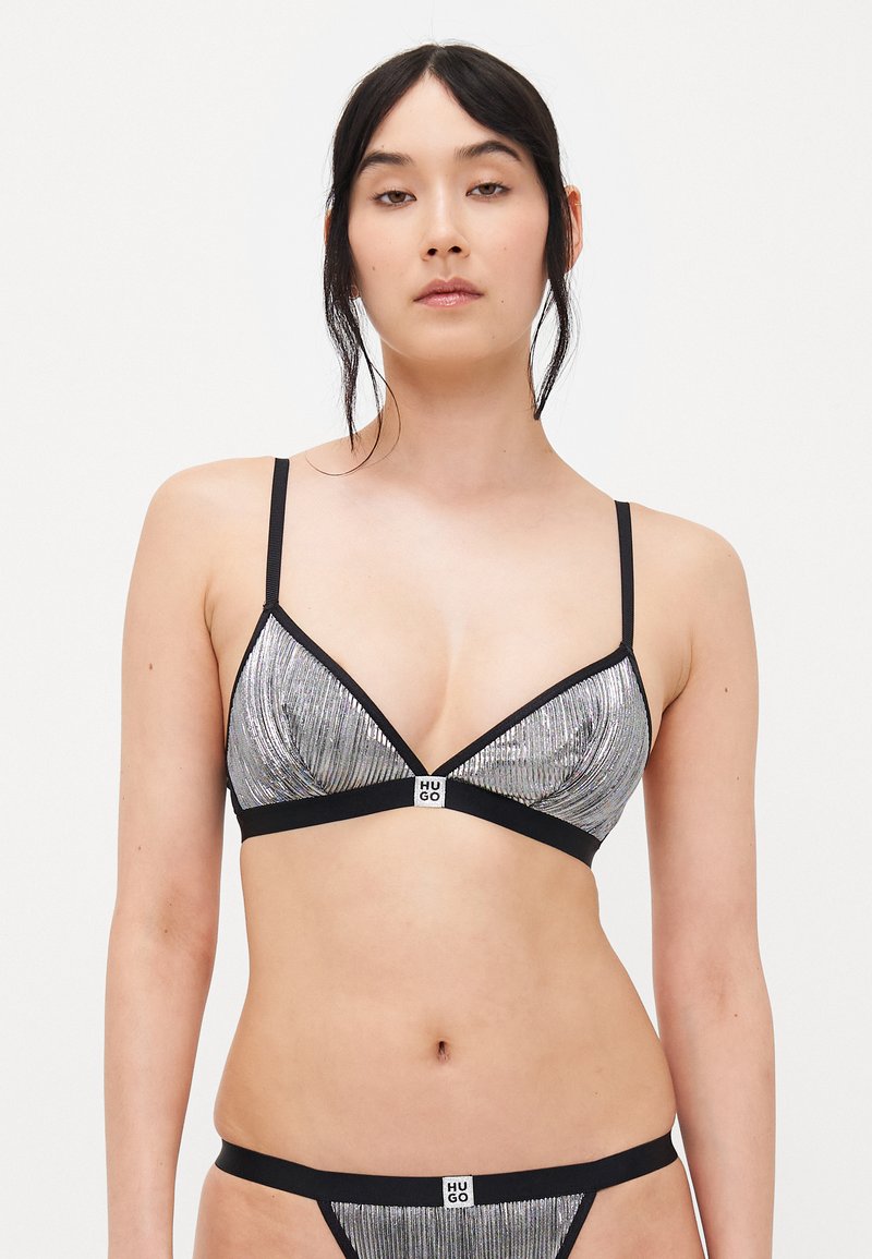 Soutien-gorge triangulaire argent et noir avec des fines bretelles, arborant un tissu texturé et brillant ainsi qu'un détail de logo au centre.