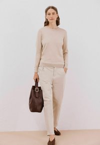 Hellbeige Strickpullover, cremefarbene Hose mit seitlichen Taschen, braune strukturierte Tragetasche, braune Schuhe mit Punkten. Einfaches, modernes Design.