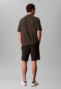 Polo à manches courtes couleur olive foncé, associé à un short noir. Le polo est en tissu texturé avec un ourlet droit. Porté avec des baskets blanches.