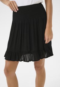 Jupe noire, longueur genou, fabriquée en tissu léger, dotée d'une taille smockée et d'un ourlet froncé. Se déplace élégamment depuis la taille.