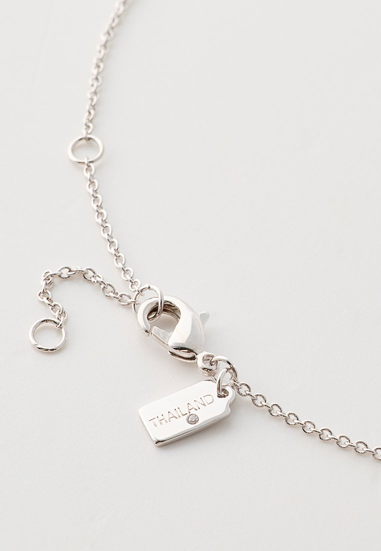 Bracelet en chaîne argentée avec un fermoir, présentant une étiquette gravée "THAÏLANDE". La chaîne est composée de petits maillons entrelacés.