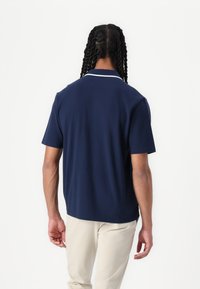 Mornarska polo majica s kratkimi rokavi, ravnega kroja, z belimi ovratniki in gladkim materialom, v kombinaciji s svetlobezž pants.