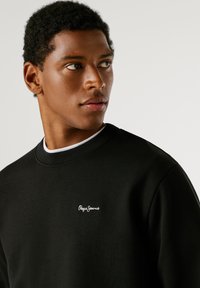 Sweatshirt preto em mistura de algodão suave, com decote arredondado, punhos canelados e um logótipo bordado em branco no peito.