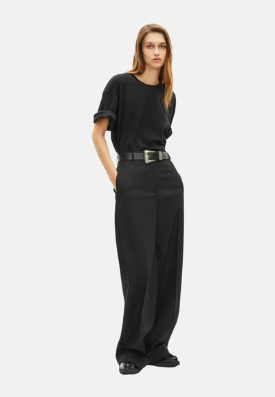Zwarte oversized T-shirt met opgerolde mouwen, gecombineerd met high-waisted, wijde broekspijpen. Zwarte leren riem met zilveren gespdetails.