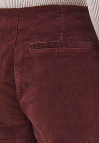 Burgundowe spodnie sztruksowe z teksturowaną powierzchnią, z tylną kieszenią i subtelnymi pionowymi liniami pochodzącymi od żeber materiału.