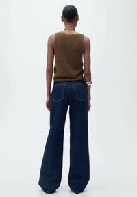 Pull sans manches en tricot marron associé à un jean en denim bleu foncé taille haute et à large jambes. Design simple avec peu de détails matériels.