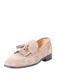 Scarpa mocassino in suede di un beige chiaro con accentuazione di nappine, cuciture a contorno e un tacco nero basso. Texture liscia; design a punta chiusa.