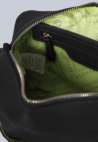 Bolso negro con cremallera y exterior texturizado. El interior cuenta con un forro verde brillante con un patrón de logotipos repetido y un pequeño bolsillo con cremallera.