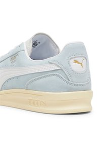 Sneaker in suede azzurro chiaro con dettagli in pelle bianca, suola in gomma crema e branding in metallo dorato sul lato e sul tallone.