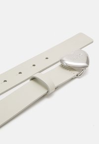 Biała skórzana opaska z wieloma otworami, z charakterystyczną, srebrną klamrą w kształcie serca z wygrawerowanym napisem "HUGO". Gładka tekstura i minimalistyczny design.