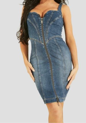 Kvinde iført en tætsiddende, ærmeløs denimkjole med lynlås foran fra buste til kant, poserende med hænderne nær hofterne.