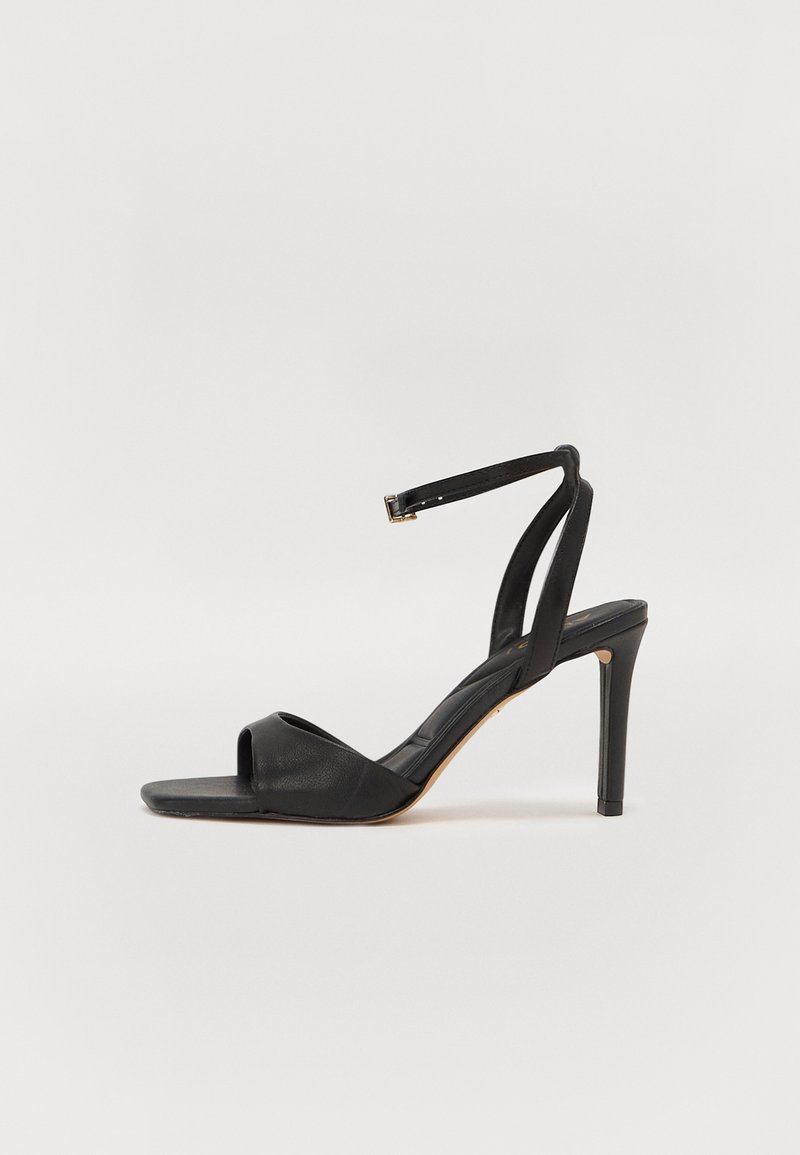 Schwarze Leder Absatzsandale mit offener Zehe, schlankem Knöchelriemen und Stiletto-Absatz. Glatte Textur und minimalistisches Design.