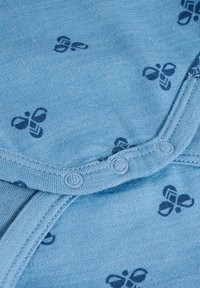 Ljusblått tyg med en mjuk yta har ett marinblått mönster av stiliserade fjärilar och två tryckknappar vid halslinningen.