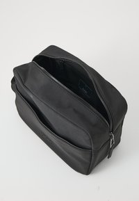 Borsa rettangolare nera realizzata in tessuto liscio, con un comparto principale con zip e una tasca frontale, con logo del marchio impresso sul lato.