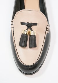 Mocassin en cuir noir et beige avec des accents dorés et des pampilles. Présente des détails cousus et une finition lisse et brillante.