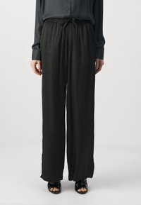 Svarta, vida byxor i mjukt tyg med elastisk midja och dragsko. Accenteras av sköna sandaler.