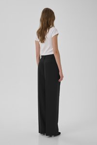 Svarta vida byxor i mjukt tyg med skräddarsydd passform, två bakfickor och en platt frontdesign, kombinerat med en åtsittande vit topp.