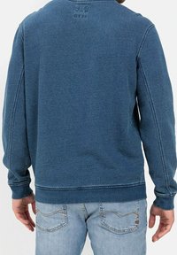 Sweatshirt in denim blu con maniche lunghe, collo rotondo e polsini a costine. Presenta cuciture a vista e un dettaglio con logo sul retro.