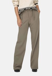 Pantalons larges en tissu beige à texture lisse, dotés d'une taille haute et de passants de ceinture, associés à un haut en tricot à motifs noir et blanc.