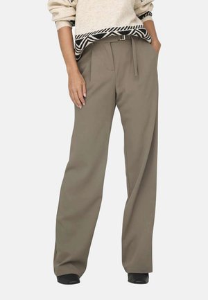 Pantalons larges en tissu beige à texture lisse, dotés d'une taille haute et de passants de ceinture, associés à un haut en tricot à motifs noir et blanc.