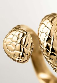 Anillo de oro con temática de serpiente que presenta una superficie texturizada con patrones de escamas, dos cabezas de serpiente estilizadas y una banda lisa.