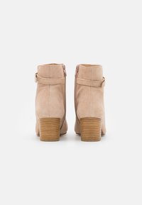 Bottines en daim beige avec un bout arrondi, fermeture à glissière et talon bloc en bois. Caractérisées par une texture lisse et un design minimaliste.