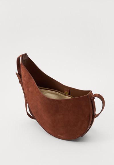 Sac à épaule en suède marron avec une forme courbée, fermeture éclair, accents en cuir et un intérieur lisse. Présente un design simple et minimaliste.
