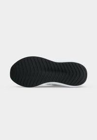 Semelle de chaussure avec motif de bande de roulement ondulé noir sur fond blanc, montrant le design de l'adhérence vu du dessous.