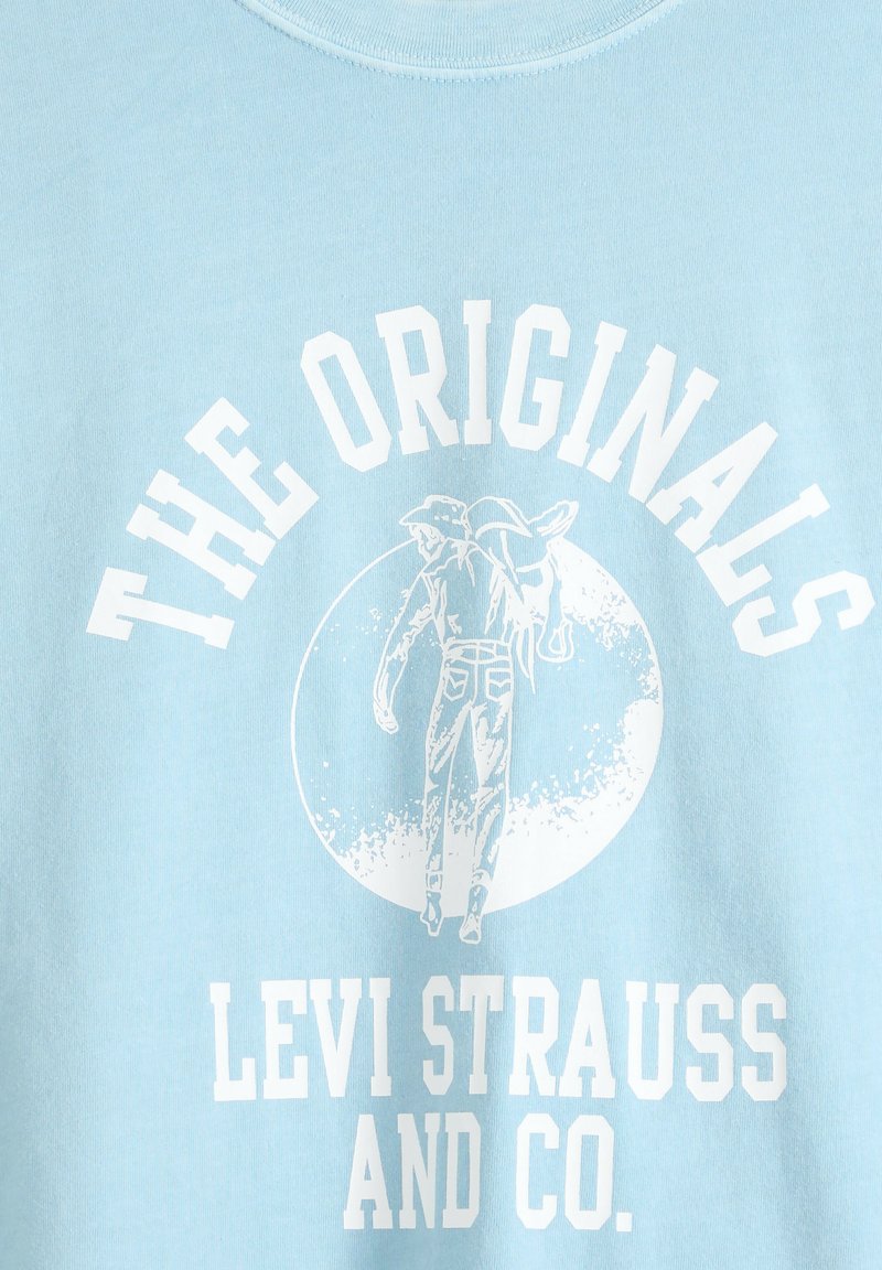 Tela azul con gráfico blanco de un hombre sosteniendo unos vaqueros sobre su hombro dentro de un círculo, texto "THE ORIGINALS" arriba y "LEVI STRAUSS AND CO." abajo.