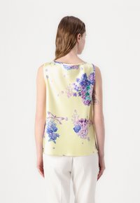 Blusa sin mangas amarilla con un acabado satinado, que presenta un estampado floral en púrpura y verde. Textura suave y corte relajado.
