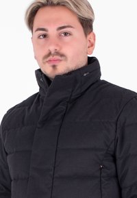 Giacca a vento nera con colletto alto, design trapuntato e chiusura con zip. Il tessuto appare liscio con accenti minimi.