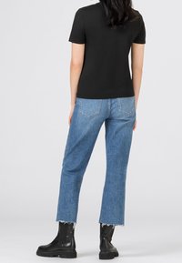 Svart t-shirt med kort ärm i kombination med ljusblå denimjeans, som har en cropped passform och fransade häm. Svarta ankelskornor fulländar utseendet.