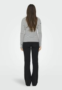 Langærmet stribet top i sort og hvid, parret med sorte flared jeans. Stof ser blødt ud; slim fit med rund hals og ingen synlige mønstre.