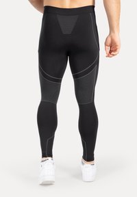 Czarne legginsy o dopasowanym kroju, z jasnoszarymi geometrycznymi akcentami i teksturowanymi panelami. Noszone z białymi butami sportowymi.