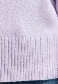 Close-up van zacht lila brei-sweaterstof met geribbelde onderrand over blauwe spijkerbroeken.