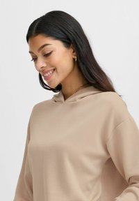 Lichtbruine hoodie met een ontspannen pasvorm, subtiele textuur en minimalistisch ontwerp. Heeft een kleine halslijn en verlaagde schouders.