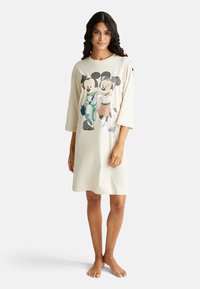 Krémový noční úbor s tříčtvrťovými rukávy. Obsahuje grafický design dvou kreslených postaviček. Vyrobeno z měkké látky.