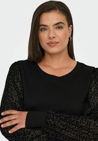 Crna majica s rebrastim tijelom, s prozirnim puf rukavima ukrašenim uzorkom leoparda tamnije nijanse crne. Dizajn s V-izrezom.