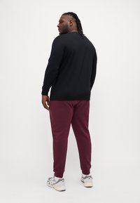 Black long-sleeve shirt paired with maroon sweatpants, viewed from the back. Shoes are light gray with cream accents. Simple, sporty design.