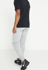 Pantalones de chándal grises con un ajuste entallado, que cuentan con una cinturilla elástica y bolsillos laterales, combinados con zapatillas negras y una camiseta negra.