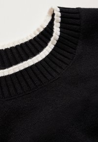 Svart tröja med en ribbad krage i svart och vitt, med mjuk tygerstruktur och rund halsringning, med fokus på den kontrasterande kragsdesignen.